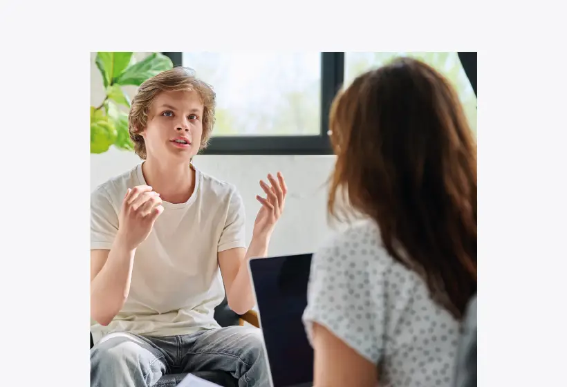 un ado assis et une adulte (assise de dos) se font face. L'adulte a un ordinateur devant elle.